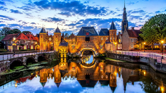 Breedbeeldfoto van de iconische Koppelpoort in Amersfoort, Nederland, met historische stadsmuren en sfeervolle verlichting aan het water tijdens zonsondergang – professionele 8K landmarkfoto voor meubels herstofferen en meubelstoffering in Amersfoort