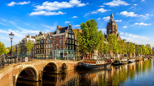 breedbeeldfoto van een historische Amsterdamse gracht met karakteristieke brug, woonboten en grachtenpanden in Amsterdam, Nederland – sfeervolle landmarkfoto voor meubels herstofferen en meubelstoffering in Amsterdam.